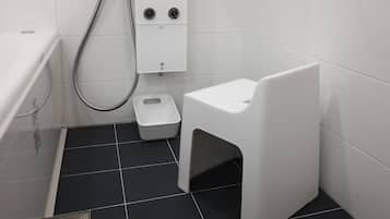 Un baño pequeño con inodoro y bote de basura blancos, y zona de ducha con ducha.
