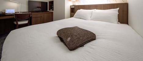 Quarto de hotel com cama, escrivaninha, cadeira, televisão e janela com cortinas estampadas.