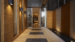 Um corredor moderno com entrada por porta de vidro, piso em azulejo e luminárias fixadas na parede.