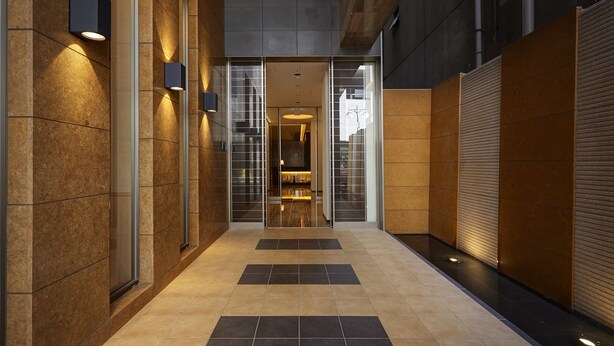 A modern hallway with a glass door entrance, tiled flooring, and wall-mounted lighting fixtures. - Hotel Forza Hakataeki Chikushi - GuchiⅠ (Fukuoka)