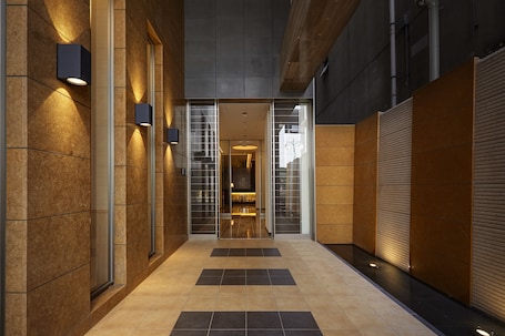 A modern hallway with a glass door entrance, tiled flooring, and wall-mounted lighting fixtures.