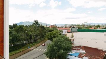 Vista de uma estrada com um carro vermelho, cercada por vegetação e edifícios.