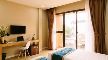 A hotel room with a wooden desk, a television, a laptop, a chair, and two beds.