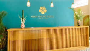 A reception desk with a teal wall, a floral logo, and three hanging light fixtures. - Minh Nhung Hotel (1 Bao Loc)