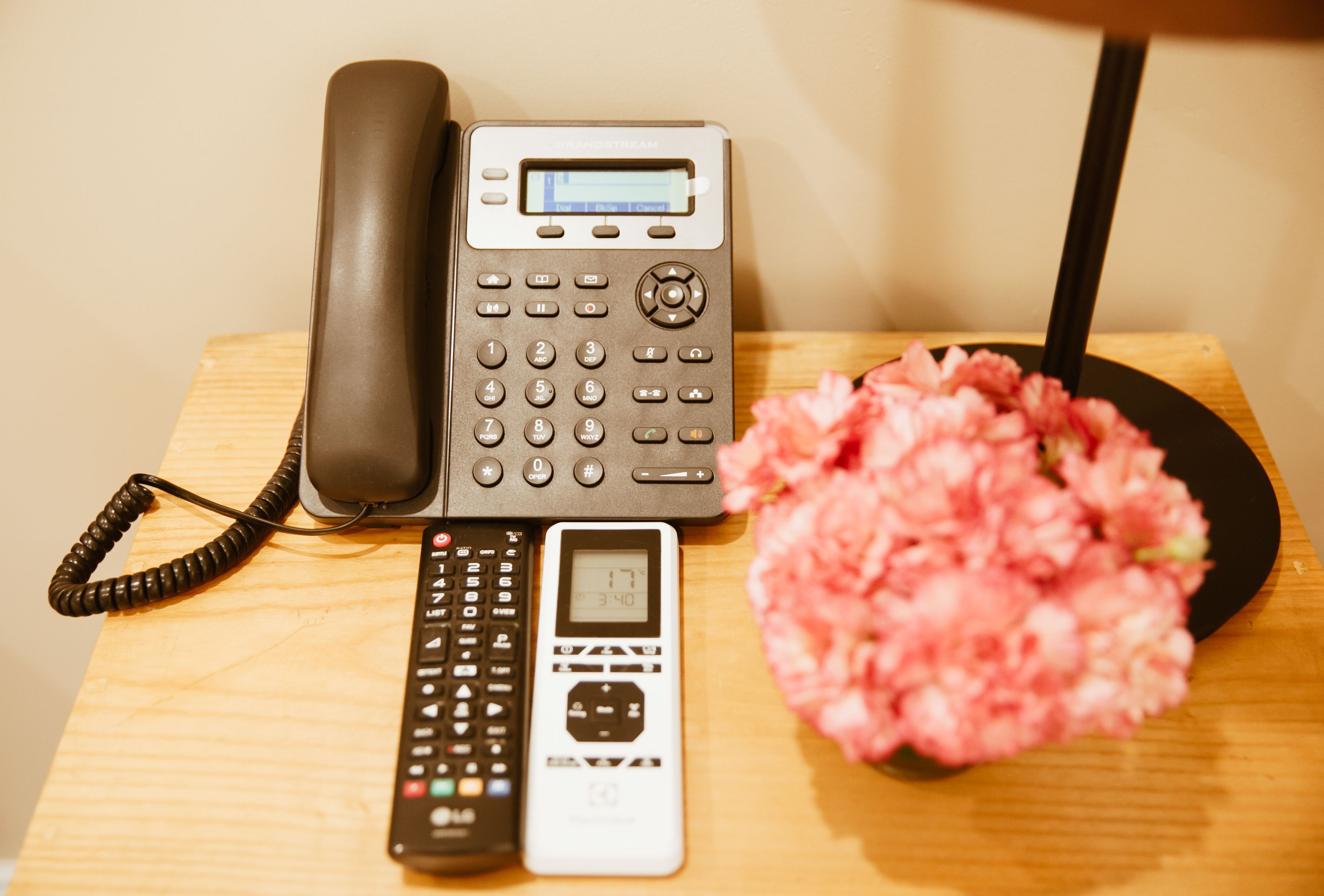 A desk with a telephone, a calculator, and a vase with pink flowers.