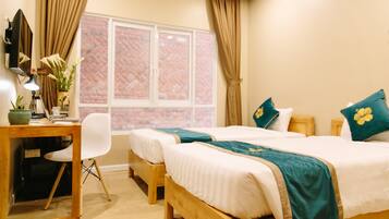 Une chambre d’hôtel avec deux lits en bois, un bureau avec une chaise, une lampe de bureau et une fenêtre avec des rideaux.