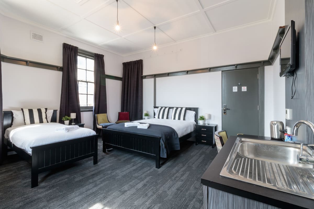 Habitación de hotel con dos camas, un lavamanos, un televisor y una ventana con cortinas.
