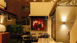 An outdoor patio area with a table and benches, string lights, and a brick building in the background. - Royal Hotel Ryde (Ryde)