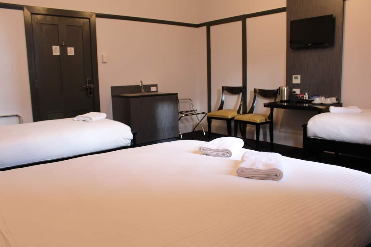 Habitación de hotel con dos camas individuales, un escritorio con silla, un televisor y una mesita con hervidor y tazas.