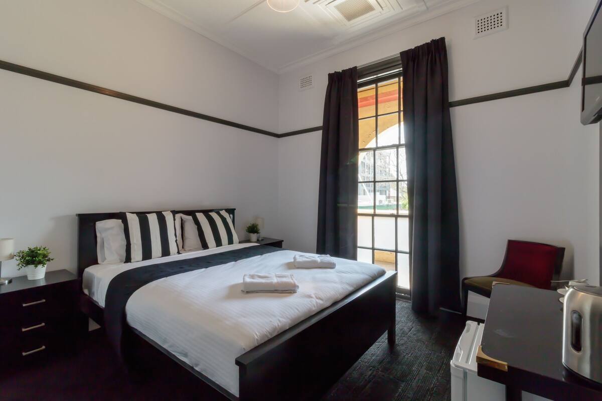 Una habitación de hotel moderna con una cama grande, un escritorio y un ventanal con cortinas.