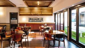 A modern restaurant interior with wooden ceiling beams, a central bar area, and large windows offering a view of the outdoor seating area. - Royal Hotel Ryde (Ryde)