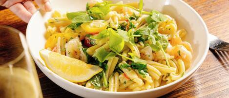 A bowl of pasta with lemon and greens on a wooden table.