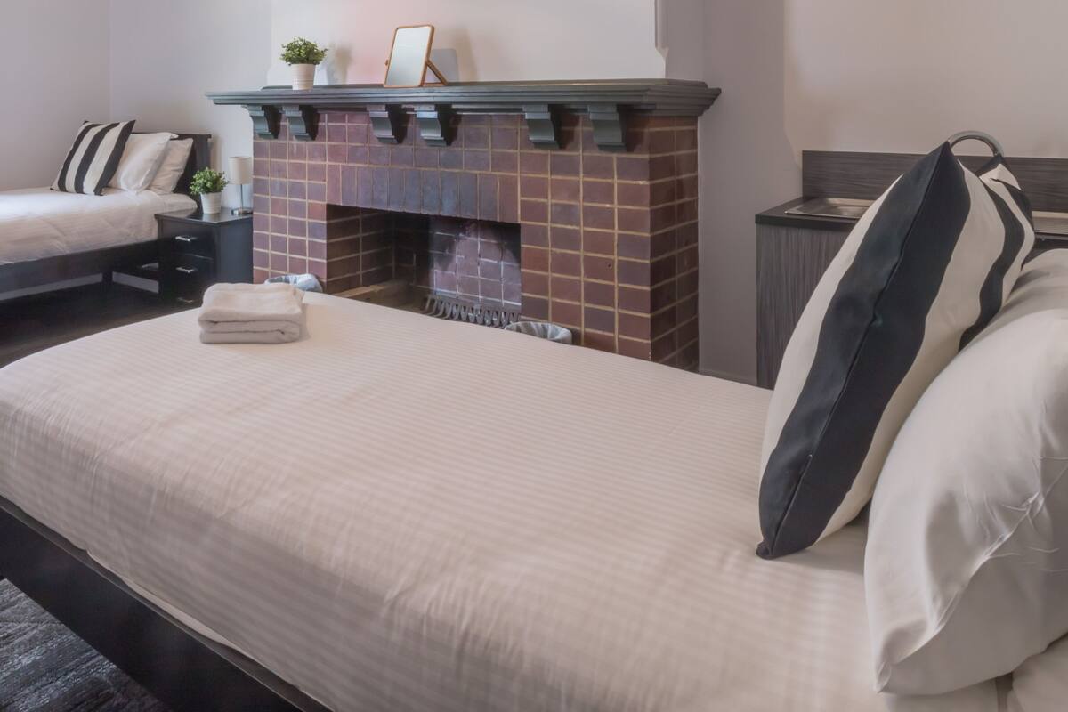 Una habitación de hotel con una cama grande, una chimenea, una mesita de noche y un buró.