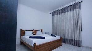 A single-bed room with a wooden headboard, white bedding, and a window with grey curtains. - The Blue Beach Guesthouse (Negombo)