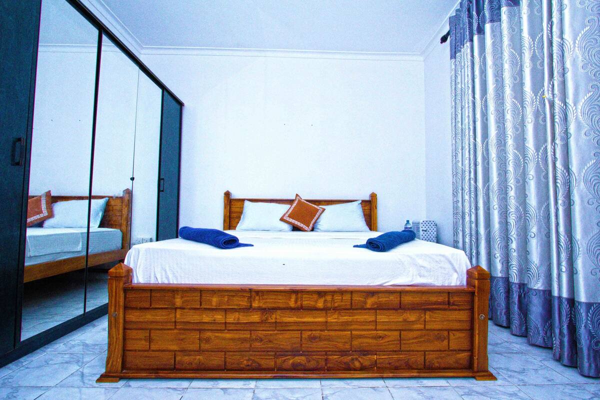 Een slaapkamer met een houten bed, een spiegel en gordijnen met een patroon.