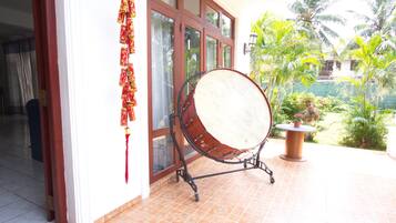 Un tambor sobre un soporte en una habitación con suelo de baldosas, una ventana con cortinas y vistas a un jardín con palmeras.