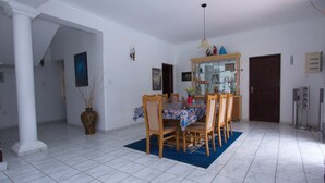 A dining area with a table set for six, surrounded by wooden chairs. A blue rug is under the table, and a chandelier hangs above. - The Blue Beach Guesthouse (Negombo)