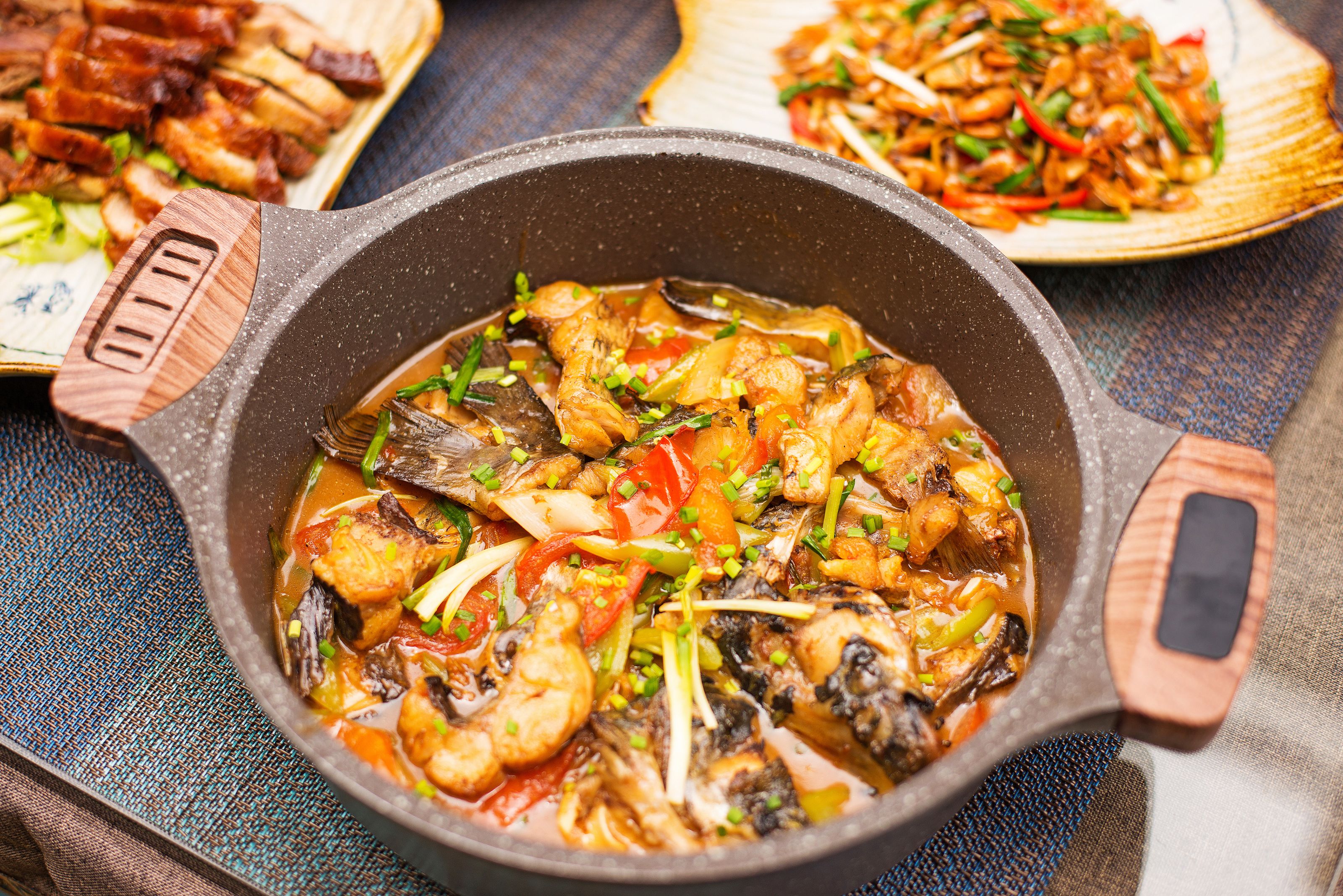 A close-up of a cast iron skillet filled with a stew-like dish, garnished with green onions and red peppers.