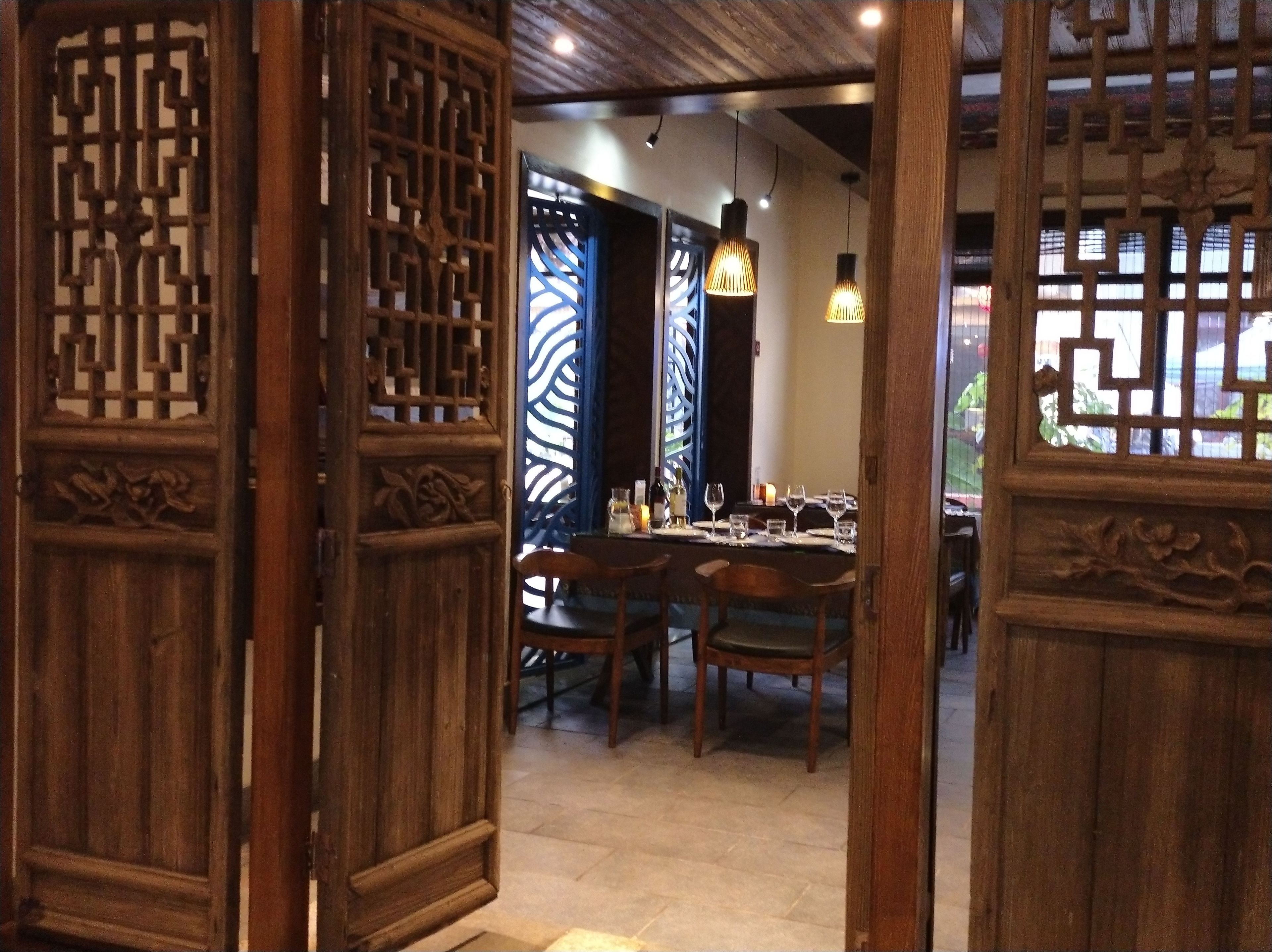 Un comedor de madera tradicional con una mesa dispuesta para dos personas, que presenta un separador decorativo e iluminación colgante.