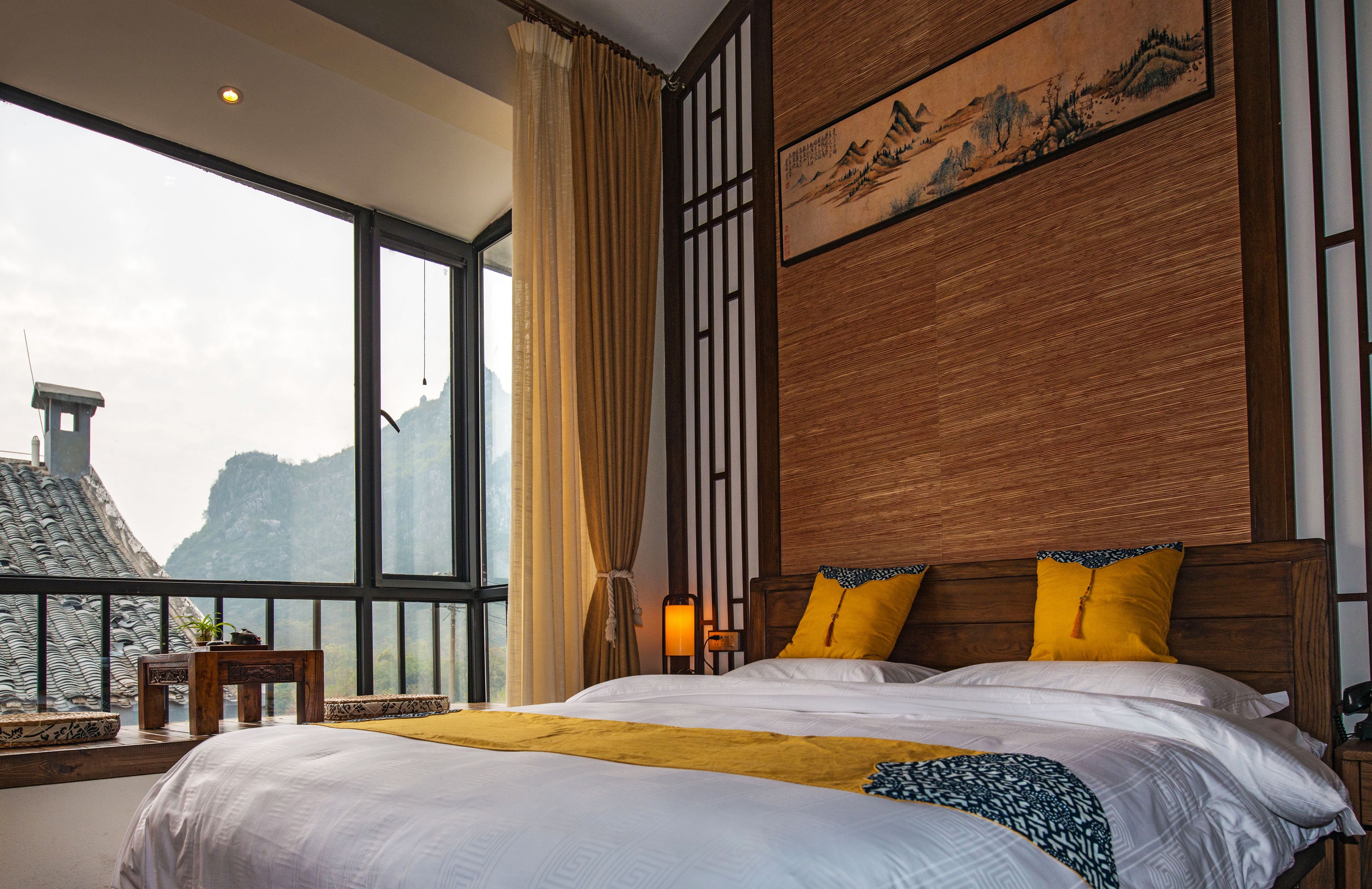 A bedroom with a large window, a bed with white bedding, and a wooden headboard.