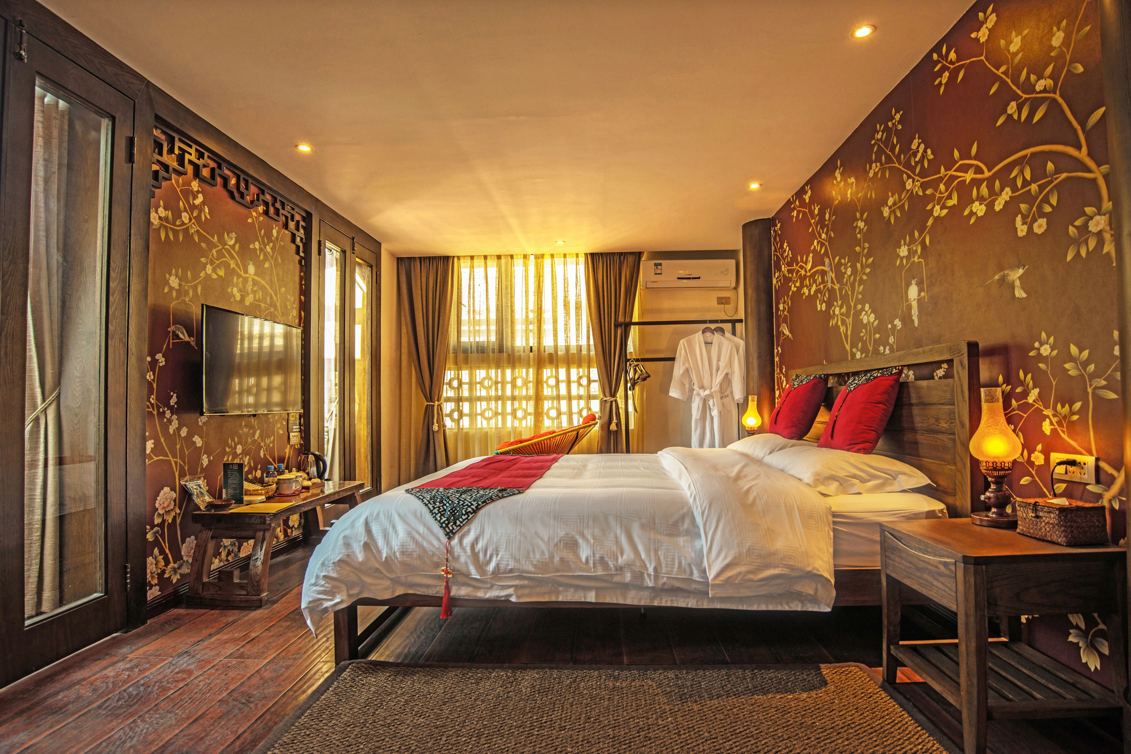 A hotel room with a large bed, a bedside table with a lamp, a TV, and a window with curtains.