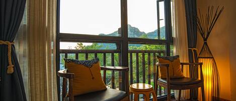 A balcony with two wooden chairs and a small table, overlooking a mountainous landscape.
