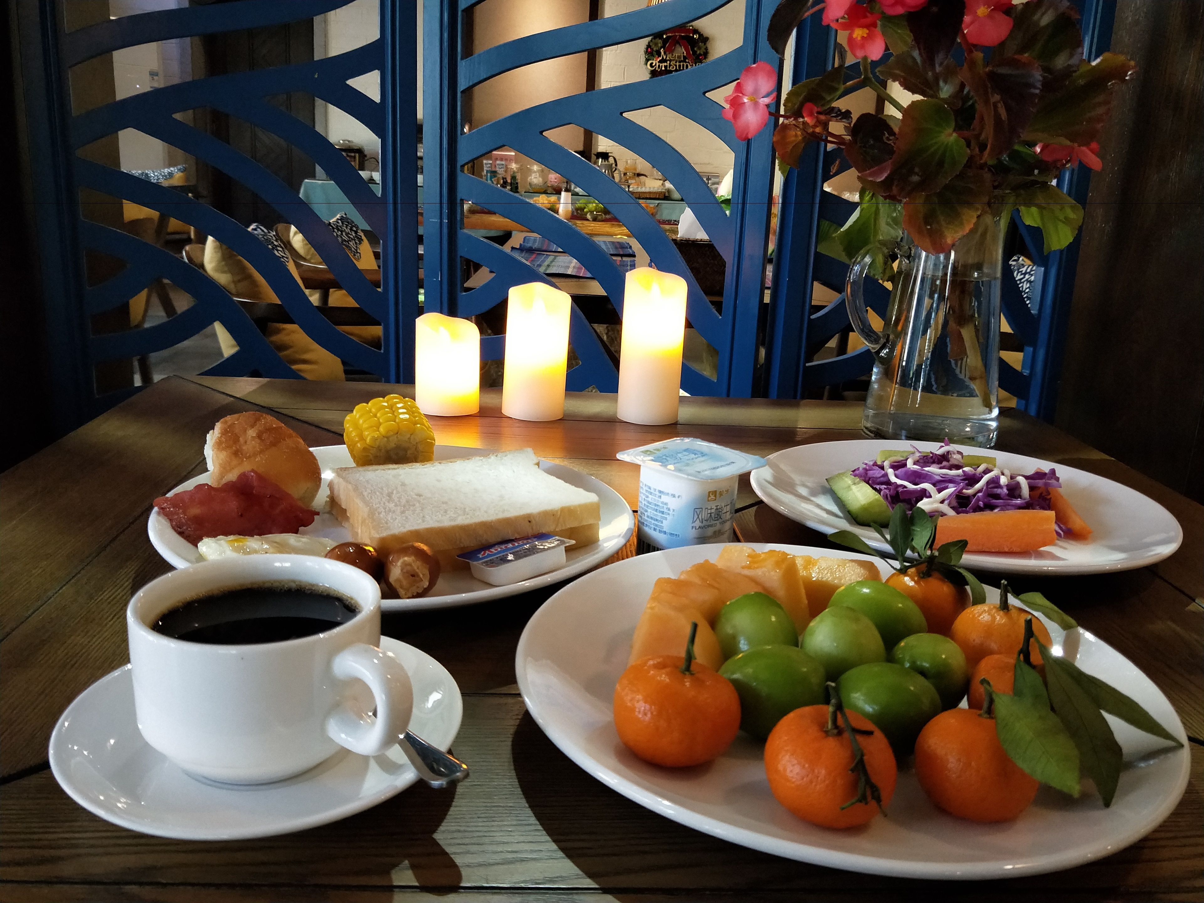 Disposição de mesa para café da manhã com xícara de café, pratos de comida, incluindo torradas, ovos e frutas, e um vaso com flores.