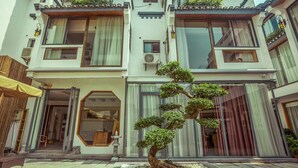A multi-story building with a traditional architectural style, featuring balconies with plants, large windows, and a well-maintained bonsai tree in the courtyard. - Secret Courtyard Resort Hotel (Guilin)