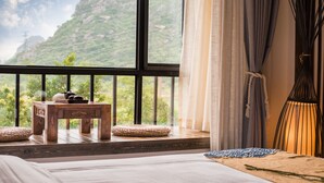 A bedroom with a large window, a wooden table with a woven basket, and a bedside lamp. - Secret Courtyard Resort Hotel (Guilin)
