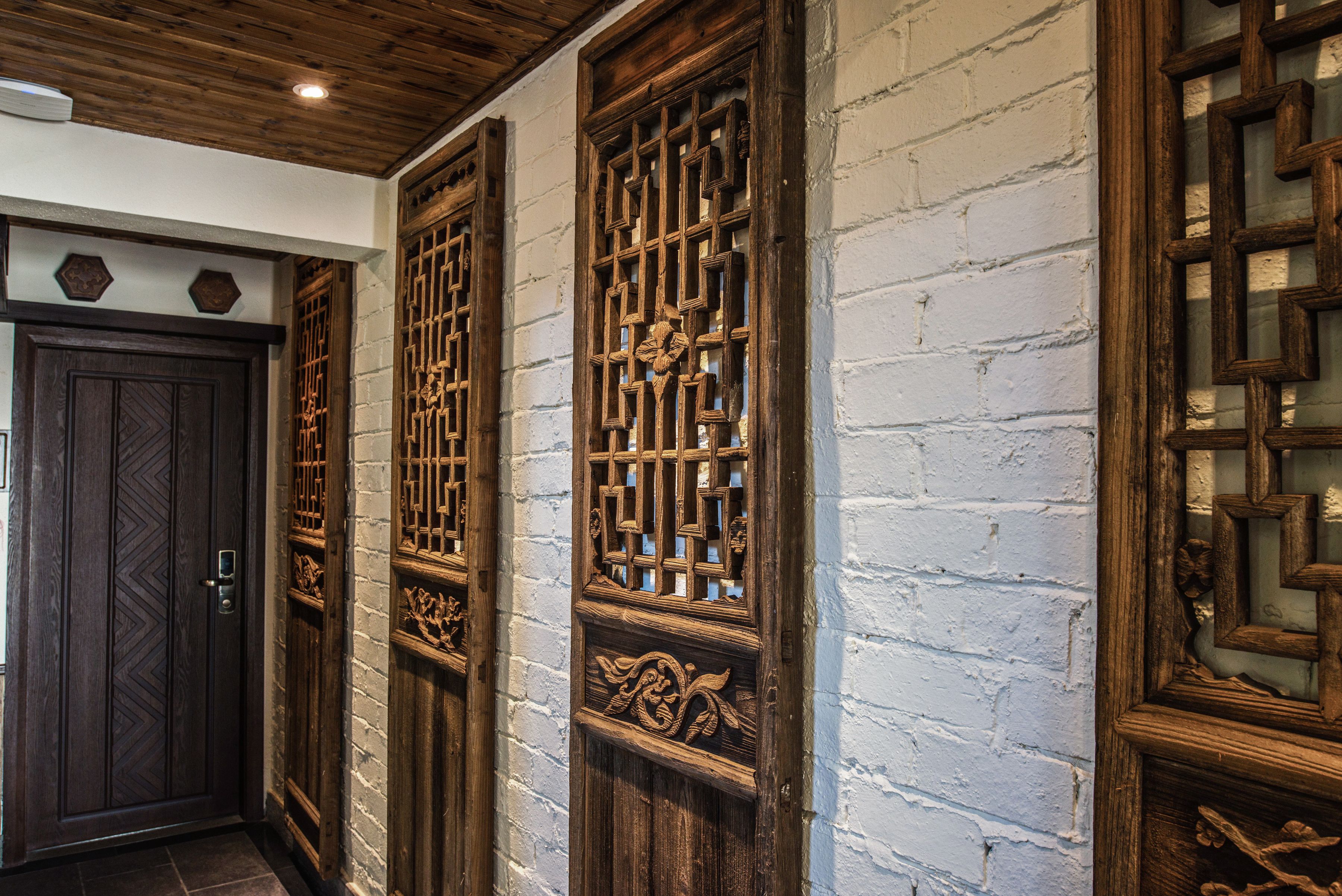 A traditional wooden door with intricate carvings, a white brick wall, and a wooden ceiling.