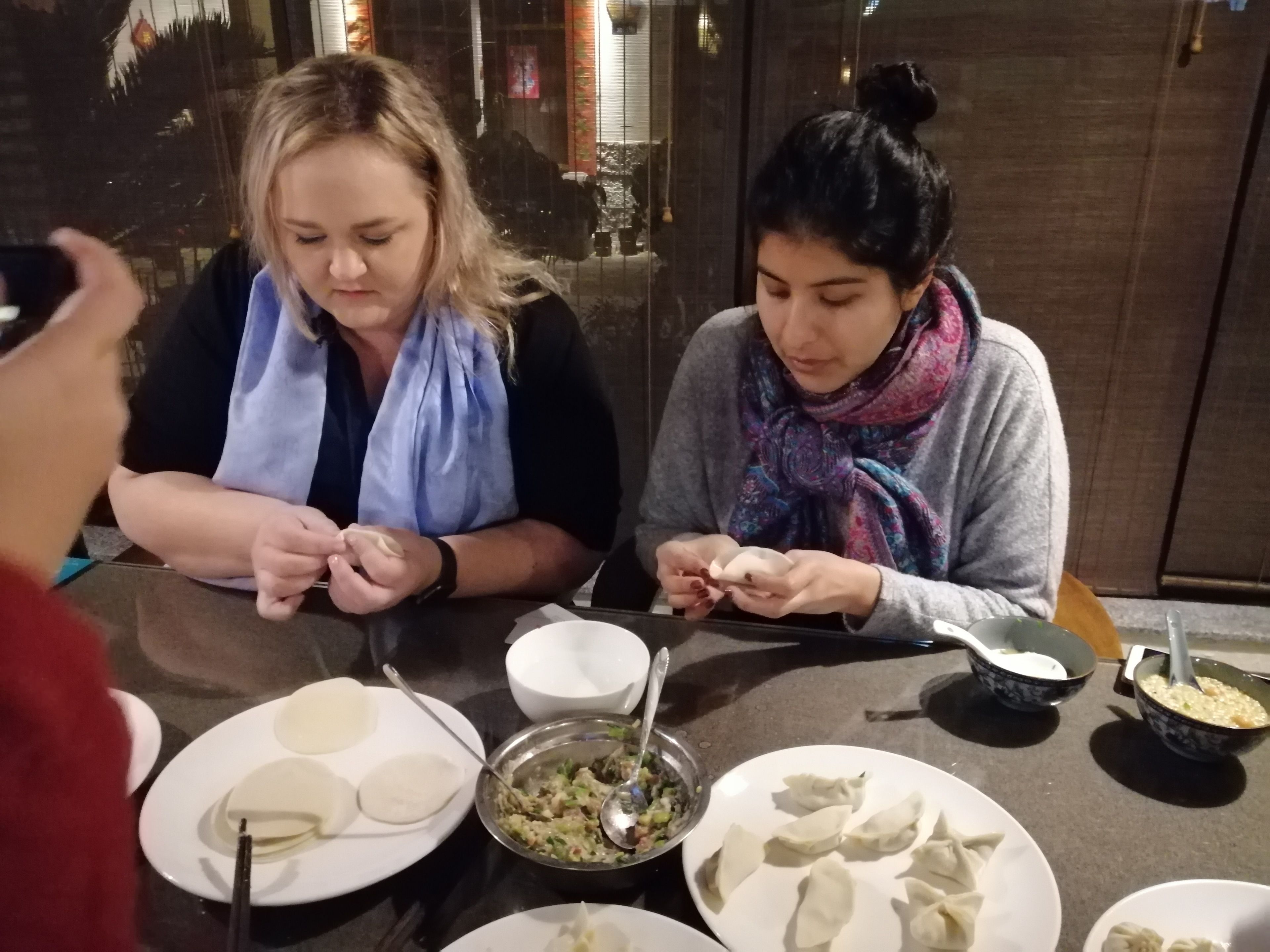 Two people sitting at a table with plates of dumplings and a bowl of soup.