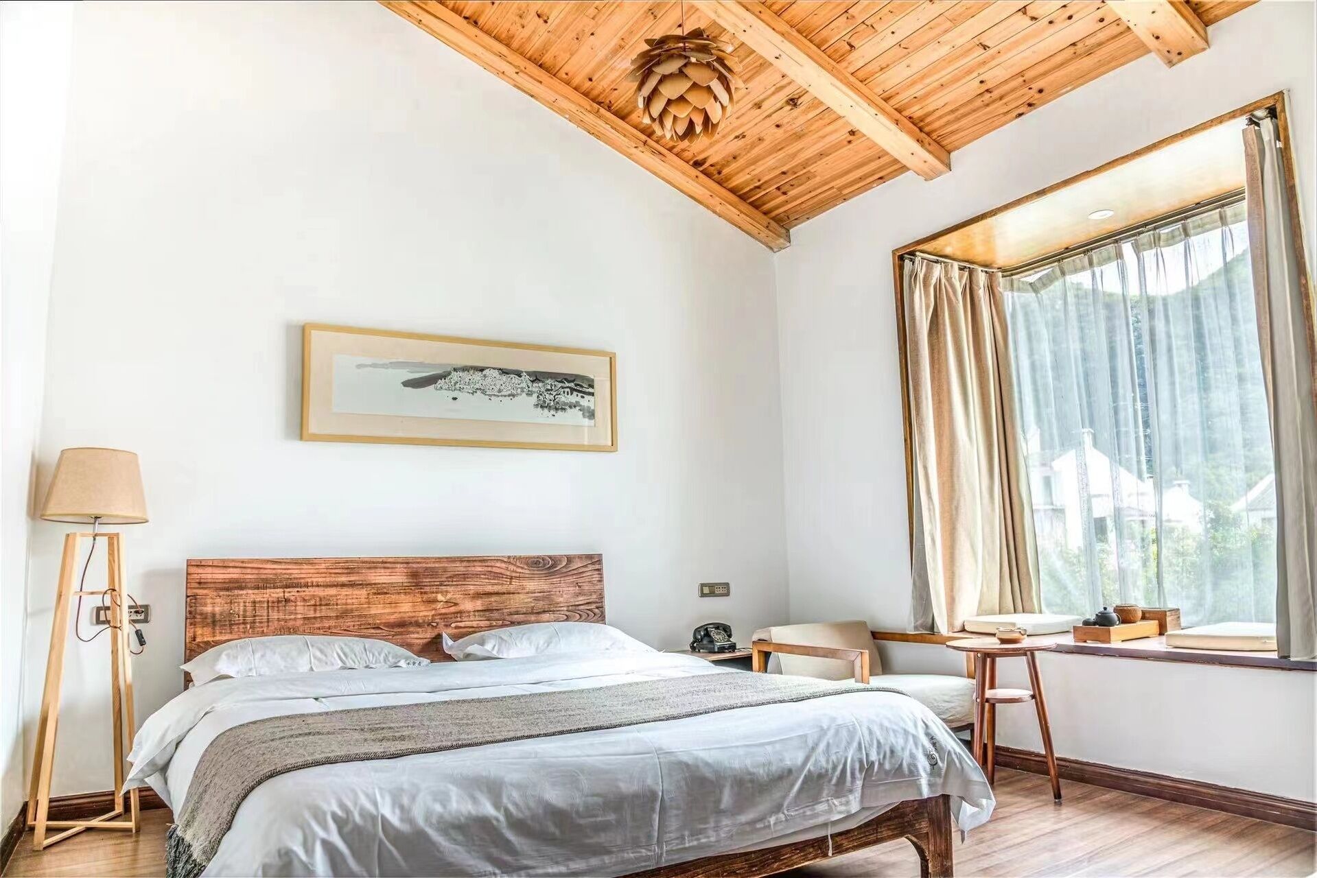 A bedroom with a wooden ceiling, a bed with white bedding, a bedside table, a lamp, a window with curtains, and a framed picture on the wall.