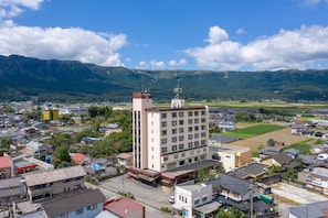 A multi-story hotel with a flat roof, surrounded by residential buildings and a mountainous backdrop. - Aso Hotel (Aso)