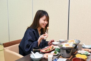 A person sitting at a table with various dishes and bowls, indicating a dining setting. - Aso Hotel (Aso)