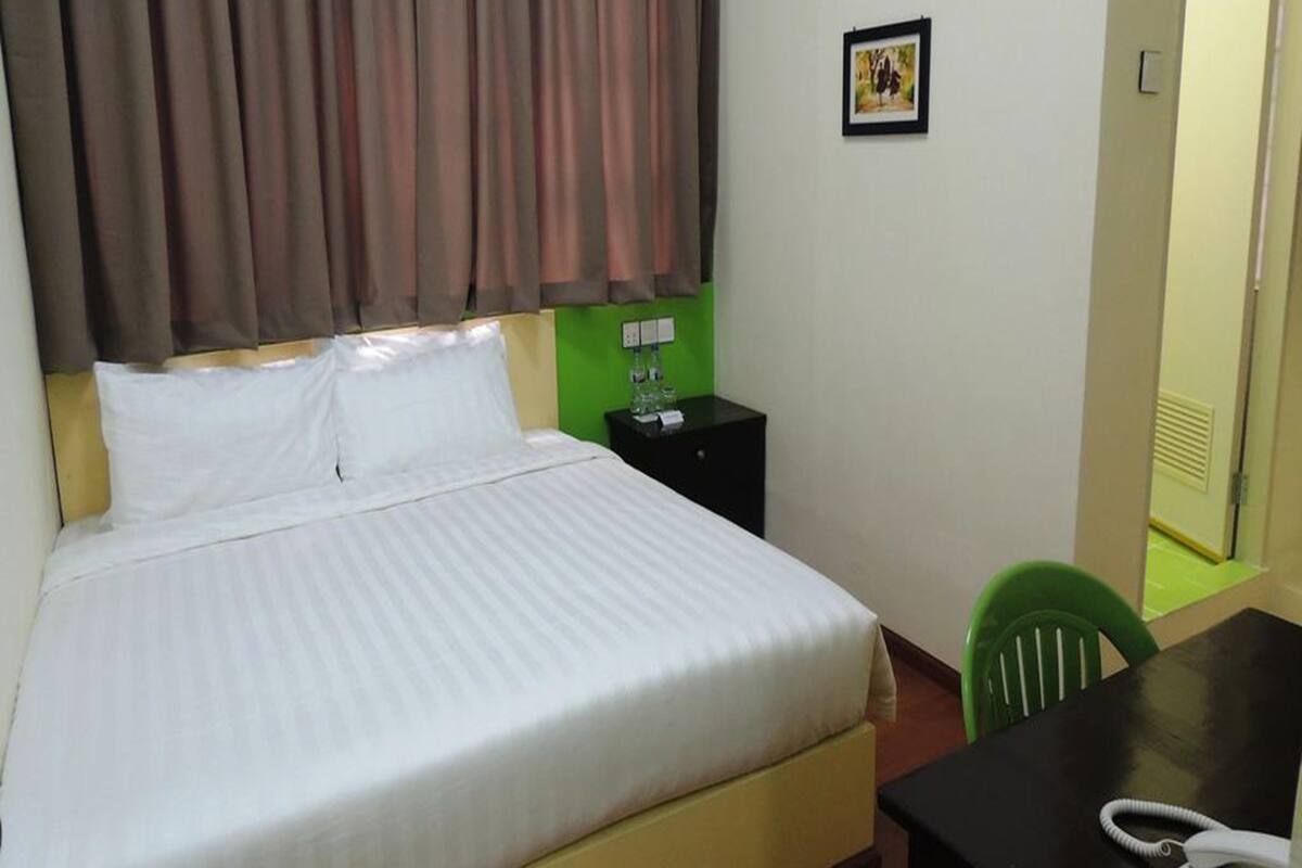 Una habitación de hotel con una cama, una mesita de noche, una silla verde y un escritorio con un teléfono.