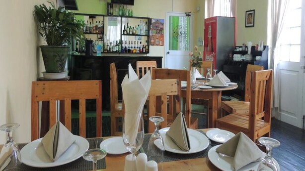 Un restaurante con mesas y sillas de madera, una zona de bar con botellas y un ventilador de techo.