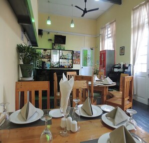 Un restaurant avec des tables et des chaises en bois, un coin bar avec des bouteilles exposées et un ventilateur de plafond.
