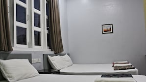 Habitación de hotel con dos camas individuales, una ventana con cortinas, un pequeño cuadro en la pared y una cama bien hecha con una toalla doblada.
