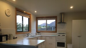 Una cocina moderna con una isla central, dos taburetes de bar, una estufa y un amplio ventanal con vistas a la montaña.