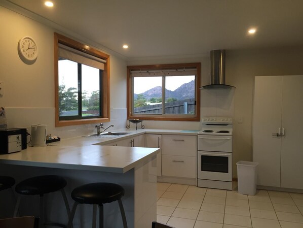 Una cocina moderna con una isla central, dos taburetes de bar, una estufa y un amplio ventanal con vistas a la montaña.