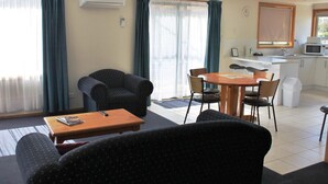 Una sala de estar con un sofá, una mesa de centro y un comedor con mesa y sillas. Se observa una cocina con microondas y fregadero.
