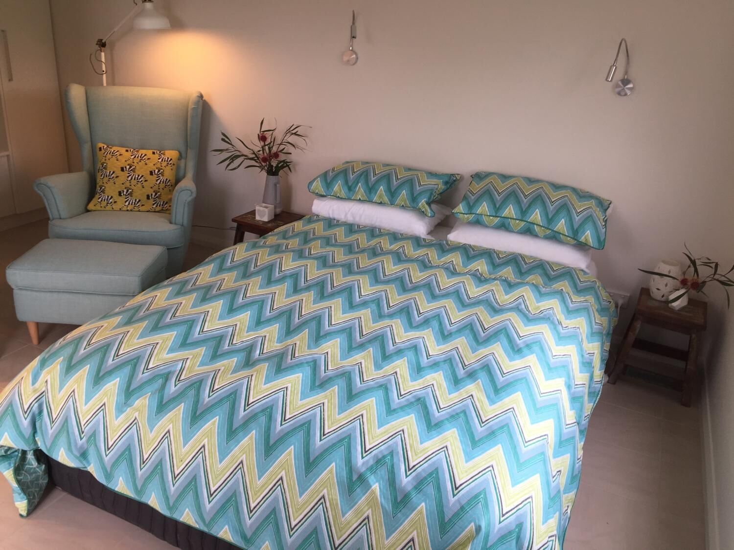 Een slaapkamer met een groot bed, een stoel, een nachtkastje en een lamp.
