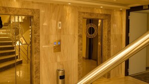 A modern hotel lobby with marble walls, a staircase, and an elevator. - Al Jamal Hotel (Amman)