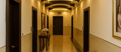 A hotel hallway with a polished floor, dark wooden doors, and a vase of flowers on a table.