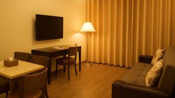 Habitación de hotel con televisión de pantalla plana montada en la pared, un escritorio con silla, un sofá con almohada y una lámpara.