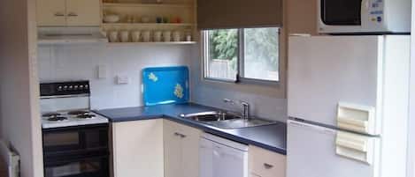 A compact kitchen with white cabinets, a stove, a dishwasher, a microwave, and a window providing natural light.