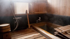 Ein traditionelles japanisches Onsen mit einer Holzwanne, einer hölzernen Sitzbank und einem Dampfrohr.