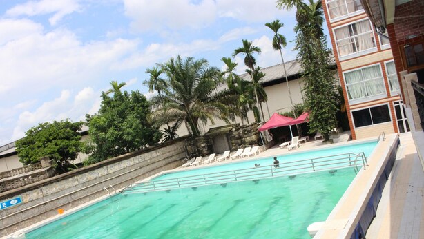 A swimming pool with clear turquoise water, surrounded by palm trees and lounge chairs. - Hôtel Belavie (Bonaberi)