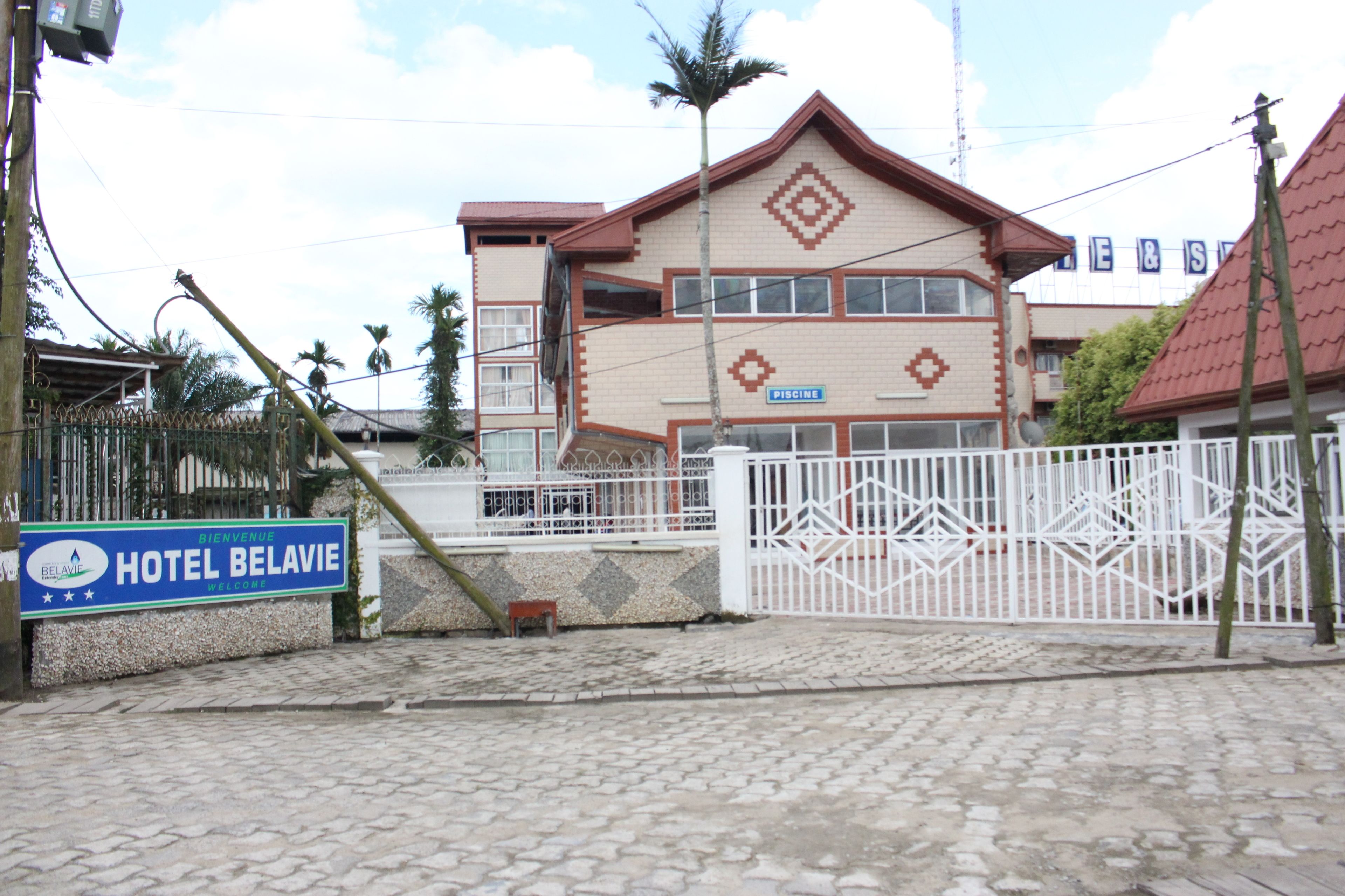 A hotel entrance with a sign reading "HOTEL BELAVIE" and a gated driveway.