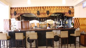 A bar area with a patterned wall, a counter, and several bar stools. - Hôtel Belavie (Bonaberi)